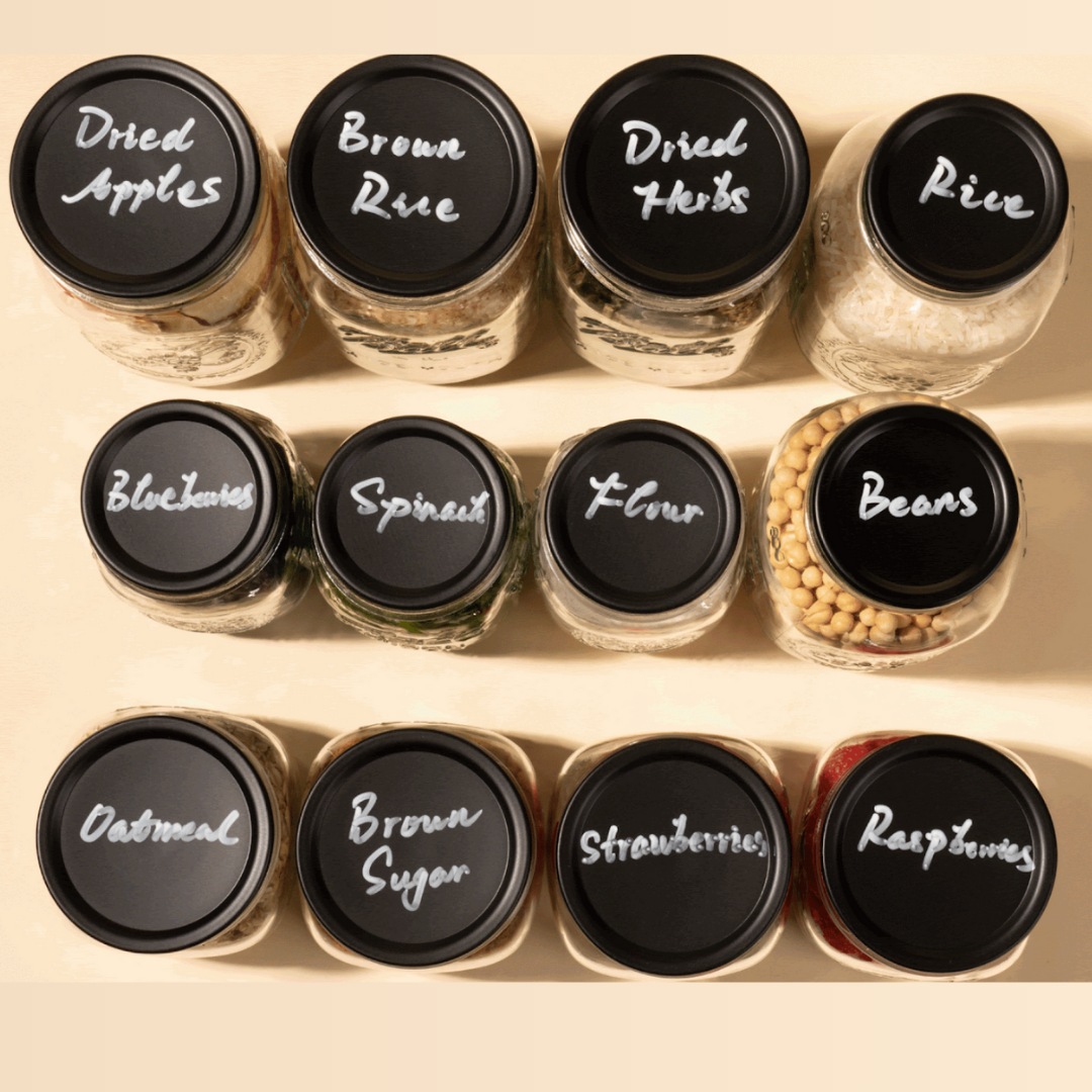 Jars with labeled black lids showing various food items, a hand writing on one lid.